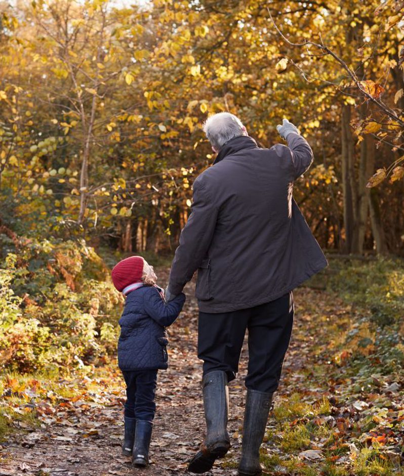 A grandfather walks in the woods with his granddaughter