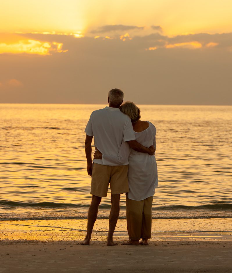 Couple embracing on beach and looking out to the sea at sunset