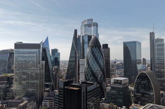 Panoramic view of a modern city skyline with tall glass skyscrapers and unique architectural towers, set against a clear blue sky.