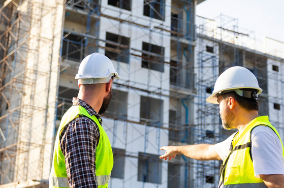 A Client ensures its project is in compliance with Building Regulations. Two men in PPE inspect a building site.