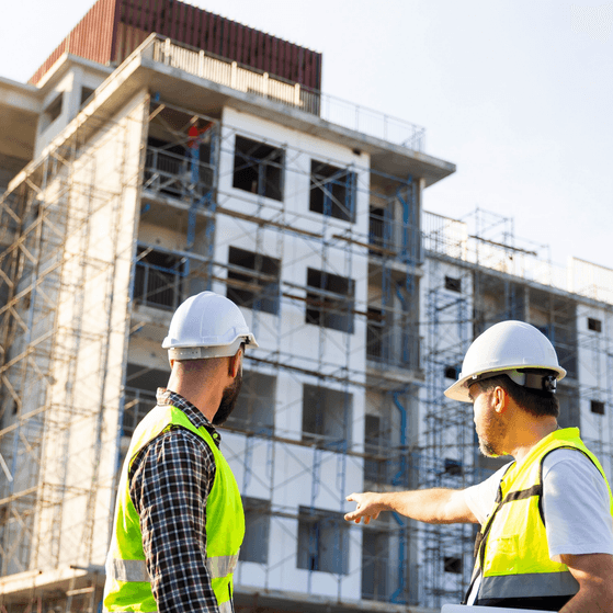 A Client ensures its project is in compliance with Building Regulations. Two men in PPE inspect a building site.