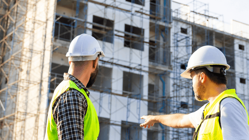 A Client ensures its project is in compliance with Building Regulations. Two men in PPE inspect a building site.