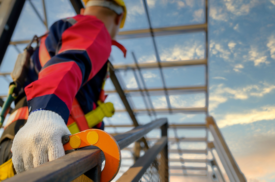 A construction worker uses a fall arrest harness on a guardrail