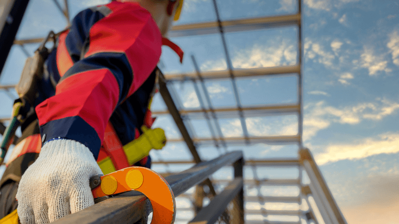 A construction worker uses a fall arrest harness on a guardrail
