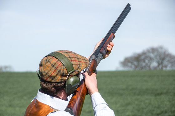 A man with shotgun and hat clay pigeon shooting