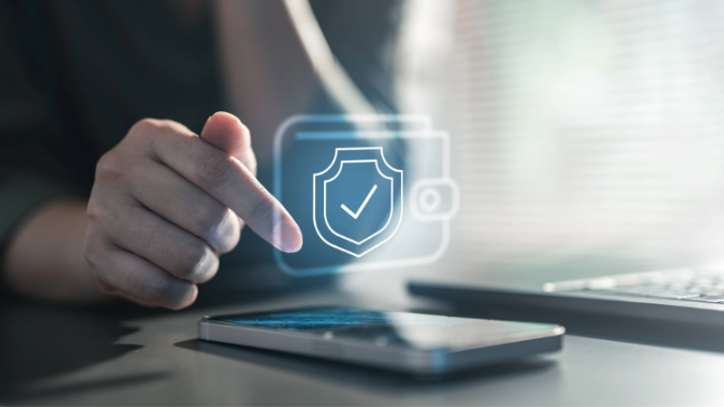 A person using a smartphone with a digital shield and checkmark icon, indicating security or protection, displayed above the device.