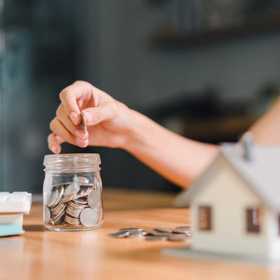 A woman fills a pot with money with a house in the foreground