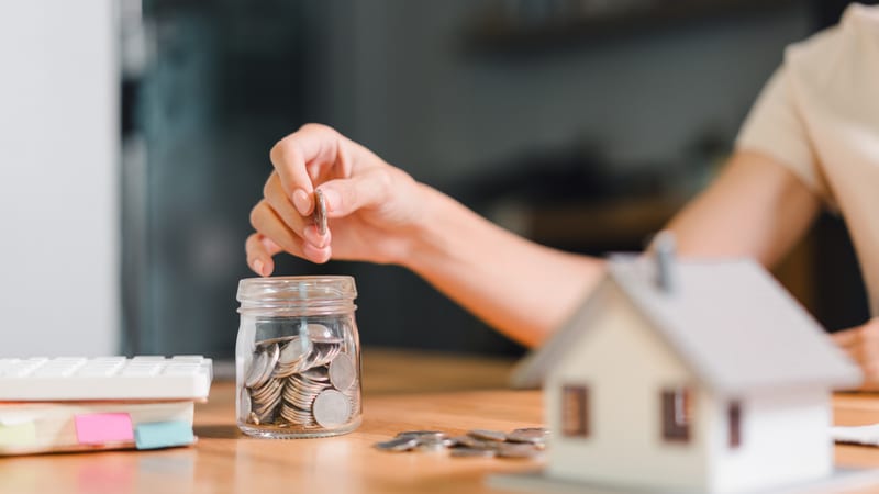 A woman fills a pot with money with a house in the foreground