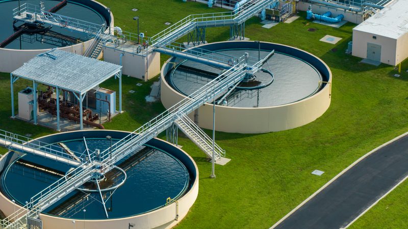 Aerial view of a water treatment plant with circular tanks, interconnected walkways, and green grass surrounding the facility.