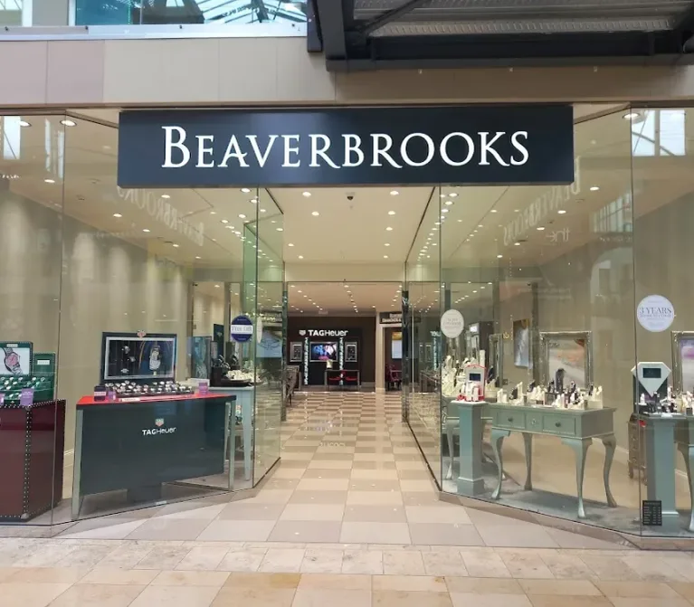 Beaverbrooks jewellery store in a mall, glass frontage and bright watch displays featuring Tag Heuer and Gucci on pale green counters and tiled floors.