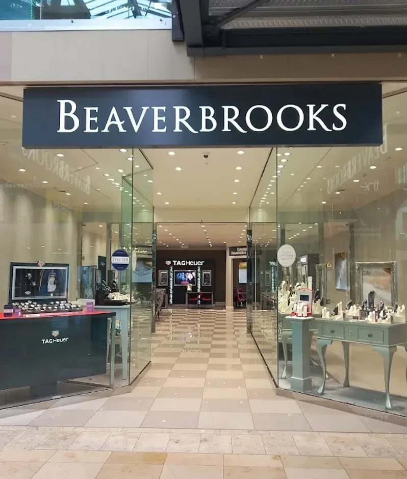 Beaverbrooks jewellery store in a mall, glass frontage and bright watch displays featuring Tag Heuer and Gucci on pale green counters and tiled floors.