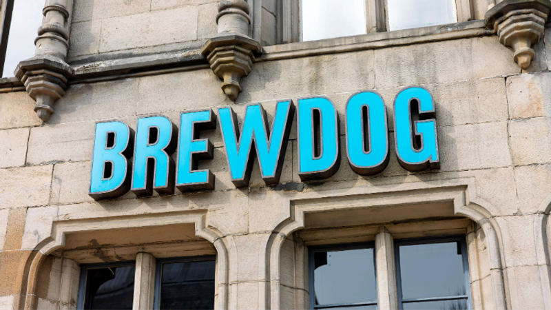 Blue 3D letters spelling BREWDOG mounted on a pale stone building facade with arched windows and decorative stonework.
