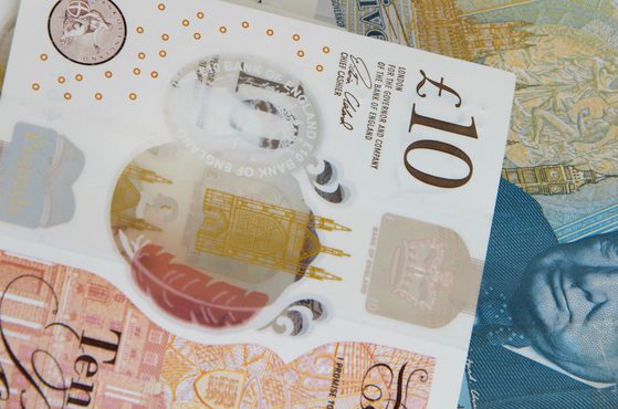 A close-up of various British banknotes, including a £10 note with a portrait of Queen Elizabeth II, and other colourful notes layered together.