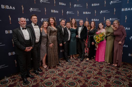 Group of formally dressed people posing for a photo at an awards event, standing in front of a blue backdrop with BiBAs logos and a patterned carpet.