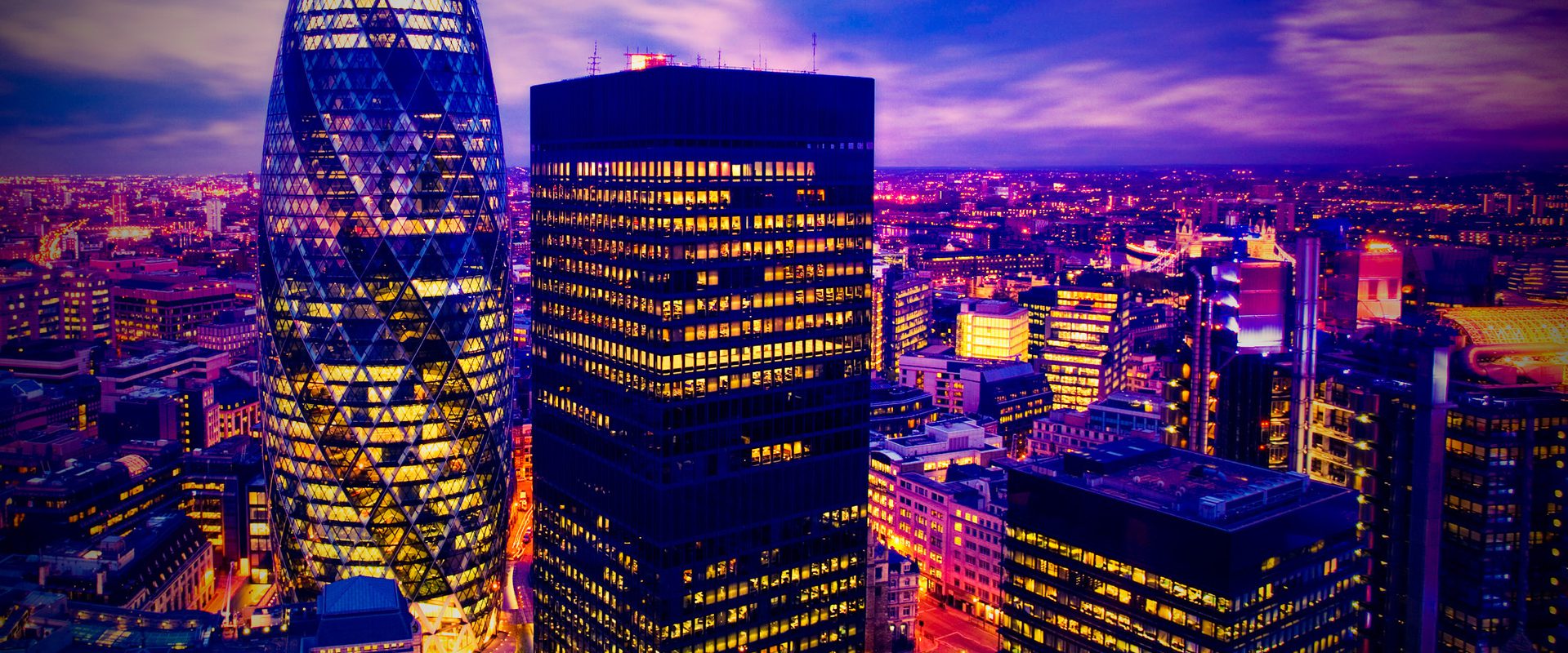 Nighttime city skyline with the Gherkin and a dark, lit office tower, streets glowing purple and gold as clouds drift over the illuminated urban expanse.