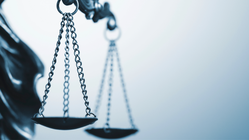 Close-up of balance scales of justice suspended by chains, with two pans in focus and a soft blue background, conveying legal fairness and measurement.
