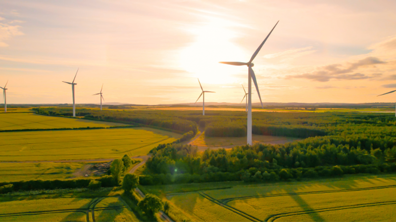 Wind turbines in a green landscape during sunset, with golden fields and a partly cloudy sky.