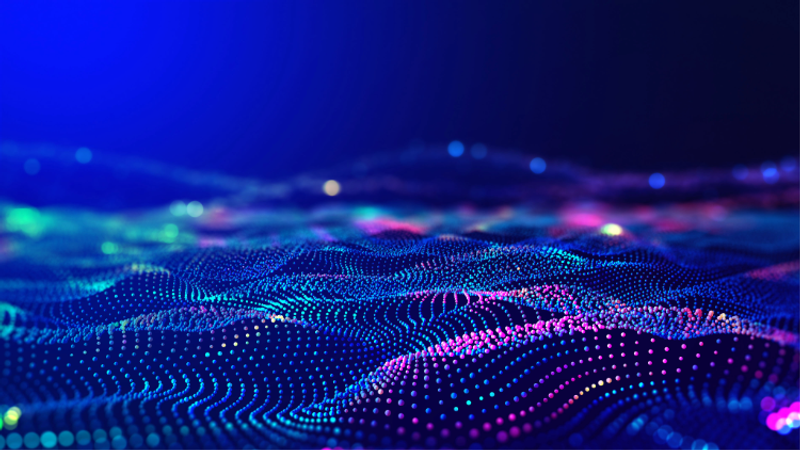 Abstract digital landscape of glowing coloured dots forming soft, wave-like dunes in blue, purple and cyan, set against a dark blue gradient background