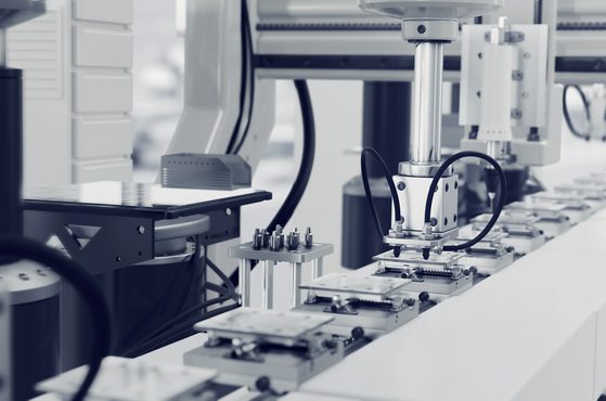 A robotic arm in a cleanroom environment, working on an automated manufacturing line with trays and machinery for precise assembly or processing tasks.