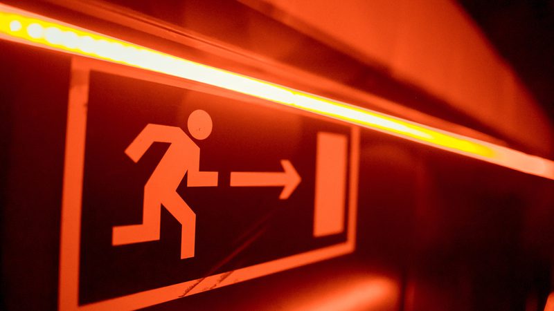A red illuminated emergency exit sign with a running figure and an arrow pointing to the right.