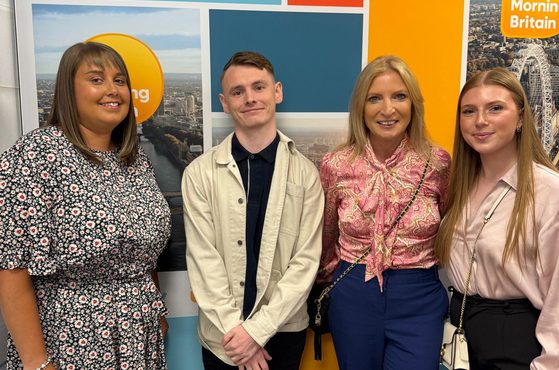 Four people standing in front of a colourful wall with "Good Morning Britain" logo, smiling and dressed in casual and smart clothing.