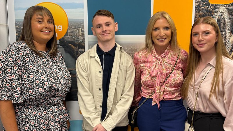 Four people standing in front of a colourful wall with "Good Morning Britain" logo, smiling and dressed in casual and smart clothing.