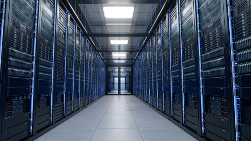 A symmetrical data centre corridor with tall server racks lining both sides, blue lighting and a distant glass door at the end.