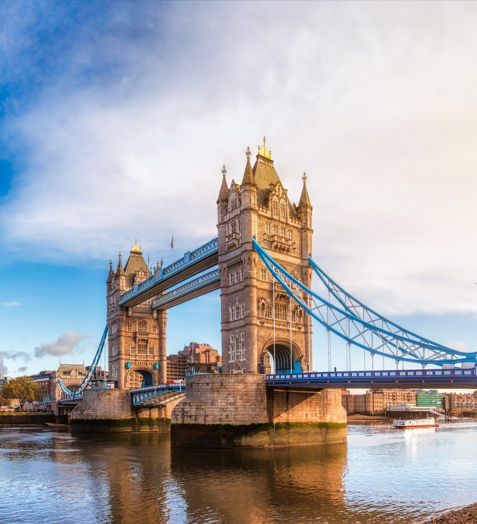 The Tower Bridge over the River Thames during daytime, with a partly cloudy sky and city skyline in the background.