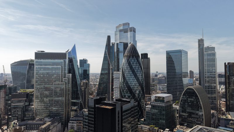 London skyline featuring modern glass skyscrapers, including the Gherkin and Walkie-Talkie, beneath a clear blue sky.