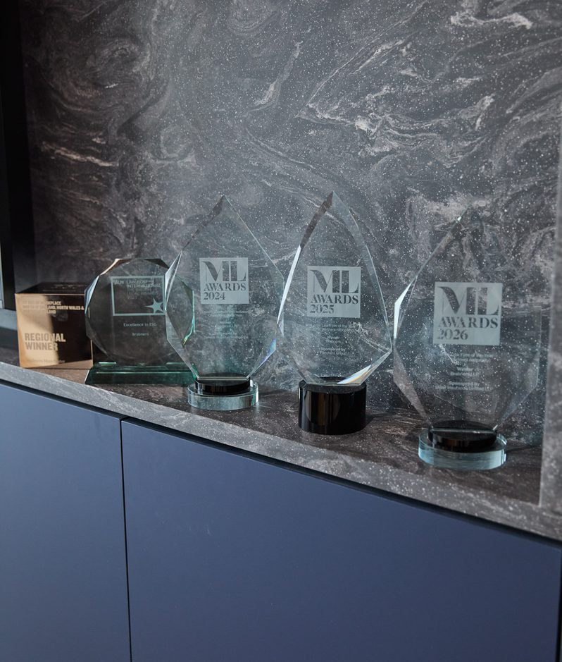 Row of faceted glass ML Awards trophies dated 2024 to 2026 and a regional winner plaque on a dark marble shelf against a marbled grey wall