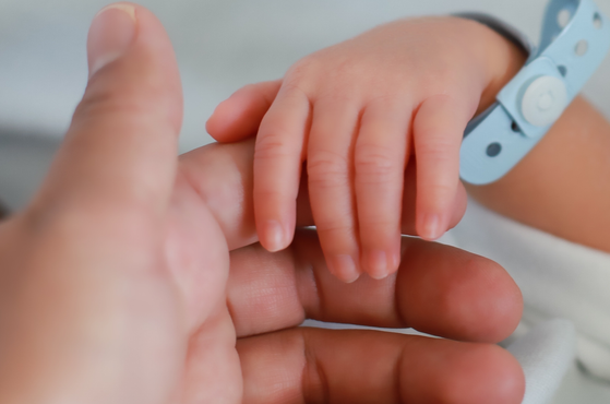 A newborn child holds the hand of its parent