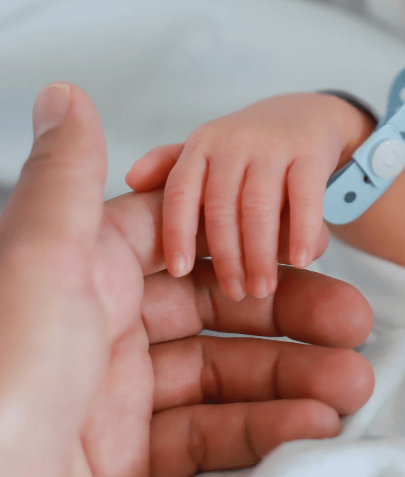 A newborn child holds the hand of its parent