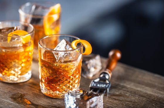 Old fashioned rum cocktail with orange zest and ice cubes