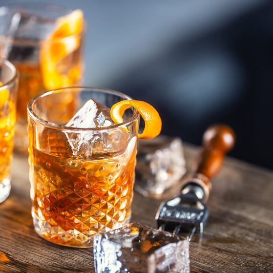Old fashioned rum cocktail with orange zest and ice cubes