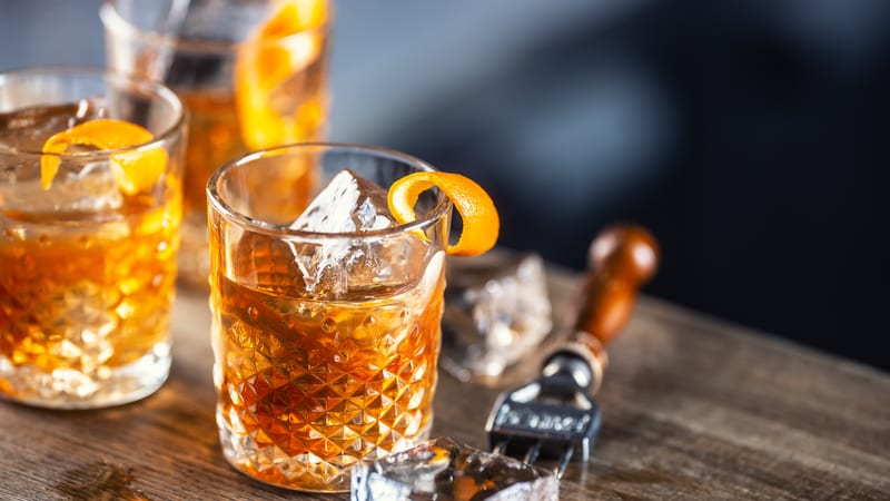 Old fashioned rum cocktail with orange zest and ice cubes