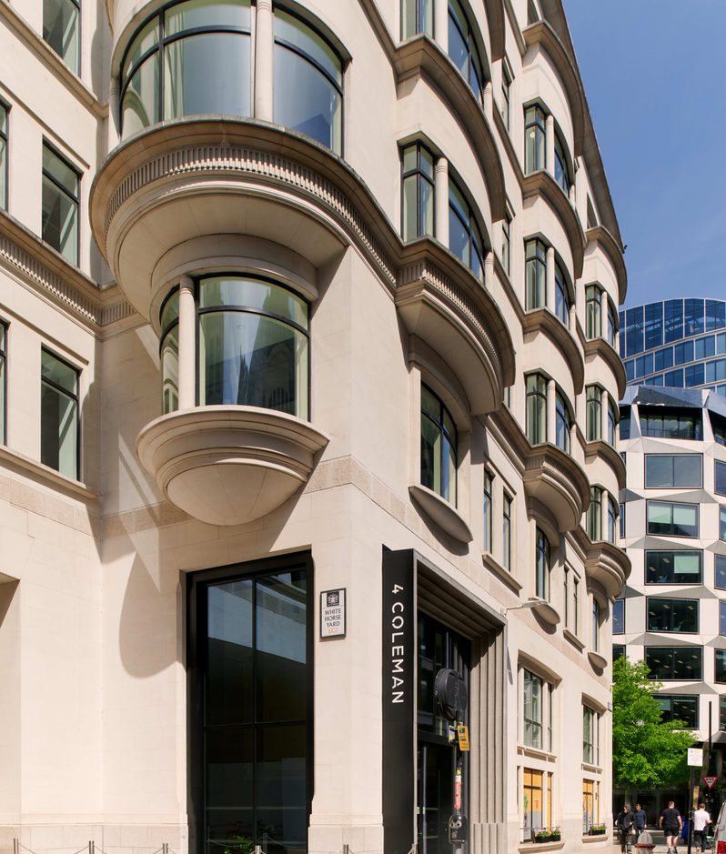 Beige stone building with rounded bay windows and curved balconies along a city street; entrance reads 4 Coleman while pedestrians walk by under a blue sky.