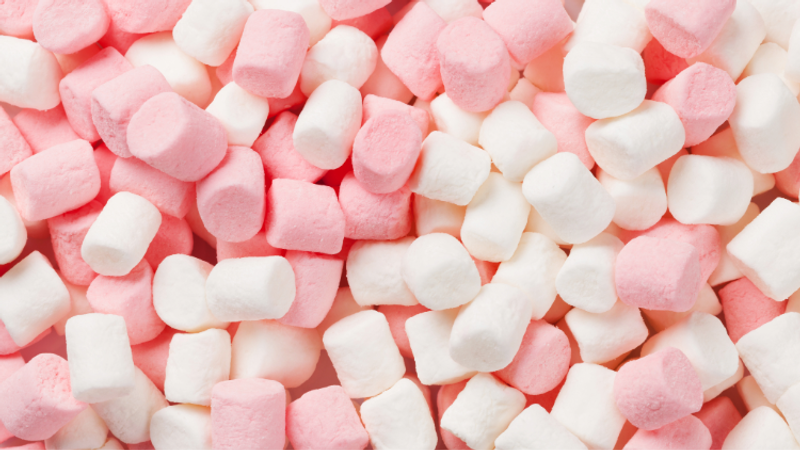 Close-up of pastel pink and white mini marshmallows scattered together, soft and fluffy, filling the frame.