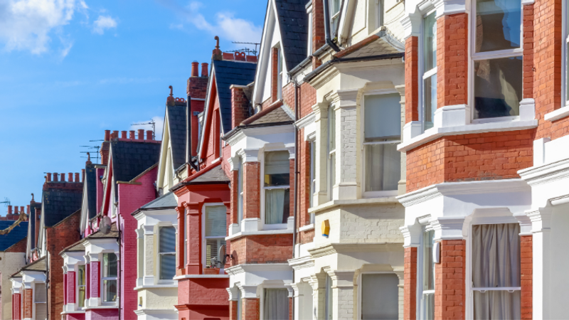 Row of colourful Victorian terraced houses with bay windows, white detailing and tall chimneys under a bright blue sky.