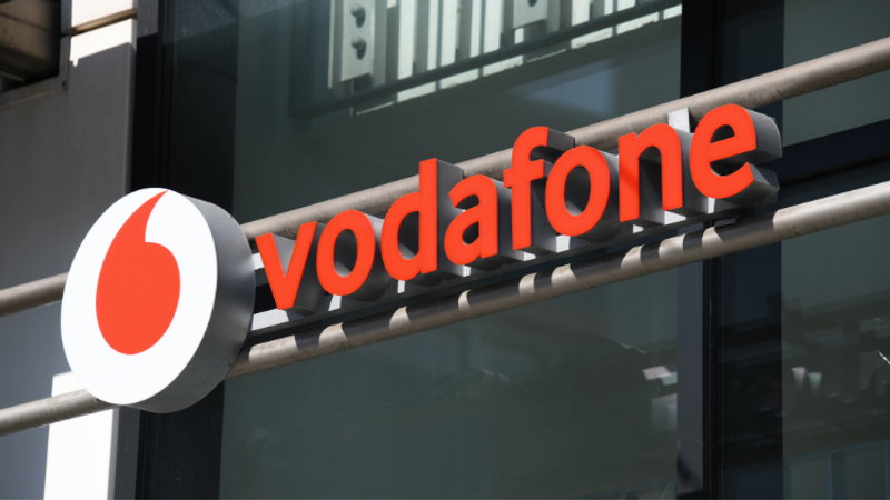 Vodafone storefront sign with bold red letters spelling vodafone and a white circular logo featuring a red teardrop, mounted on a metal frame above glass windows.