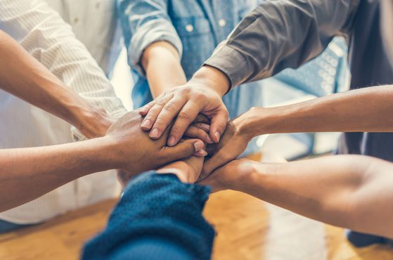 Multiple hands stacked on top of each other in a gesture of teamwork and unity.