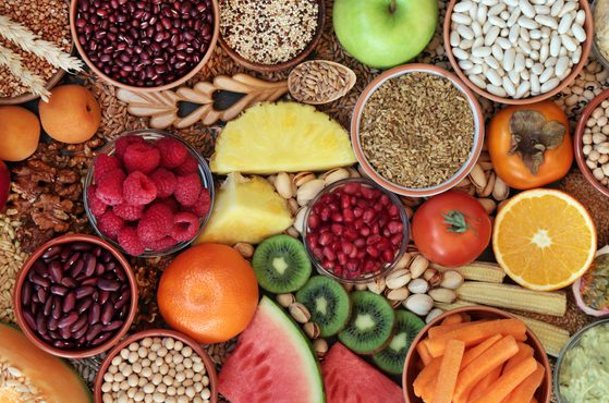Vibrant spread of fruits, seeds, nuts and grains in bowls: kiwi, orange, watermelon, pineapple, raspberries and pomegranate seeds.