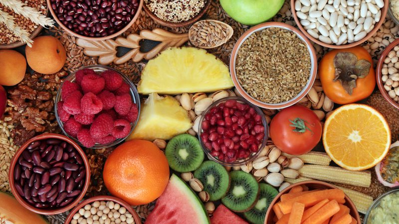 Vibrant spread of fruits, seeds, nuts and grains in bowls: kiwi, orange, watermelon, pineapple, raspberries and pomegranate seeds.