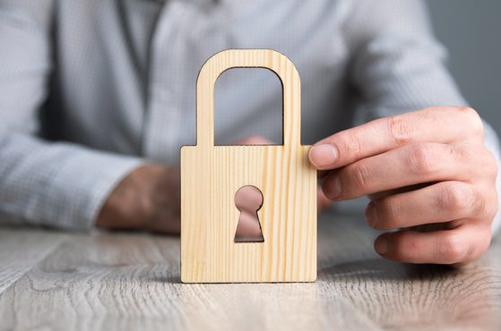 A person in a grey checked shirt holding a wooden padlock-shaped cutout with a keyhole, against a neutral background.