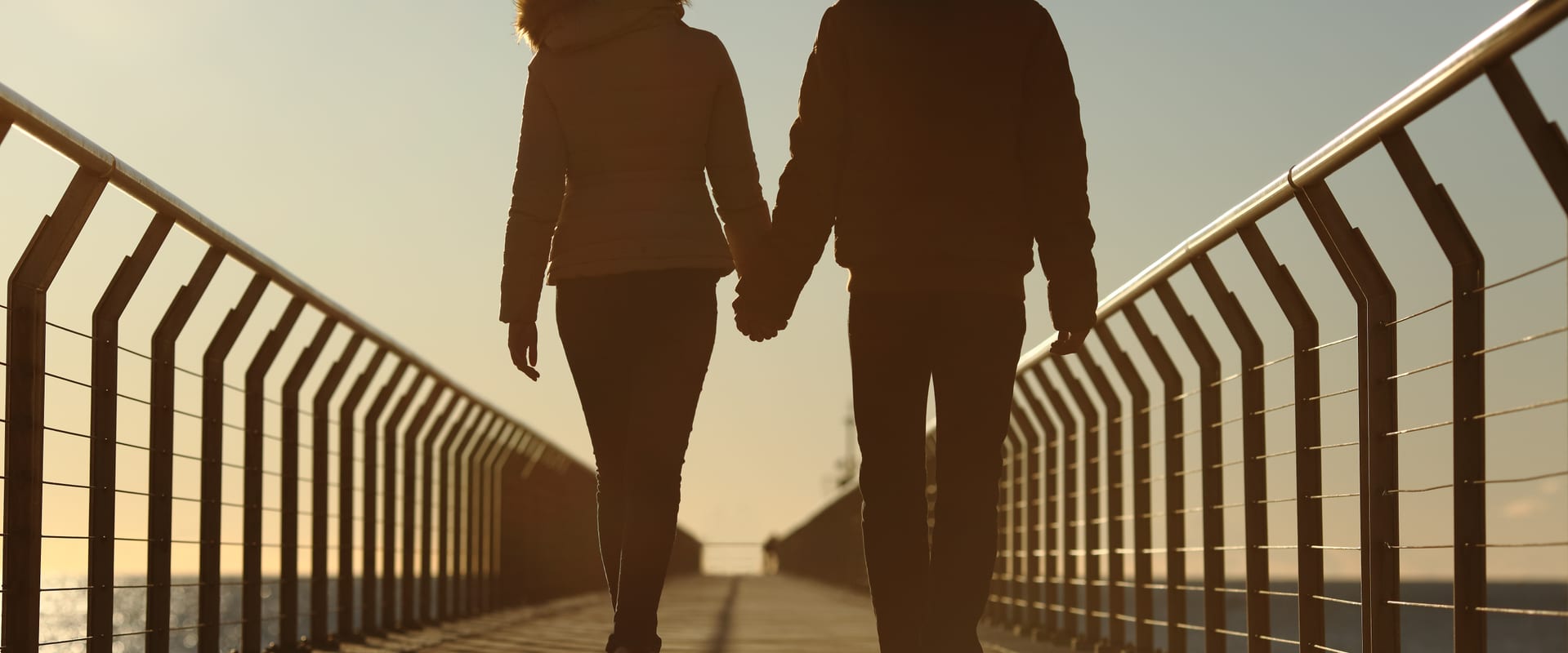 Couple walking along bridge towards ocean, scenic romantic concept
