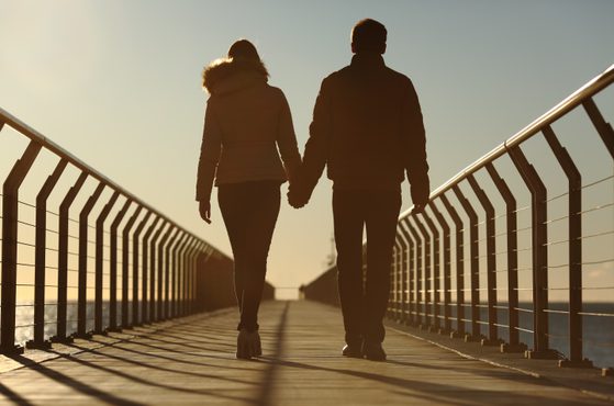 Couple walking along bridge towards ocean, scenic romantic concept