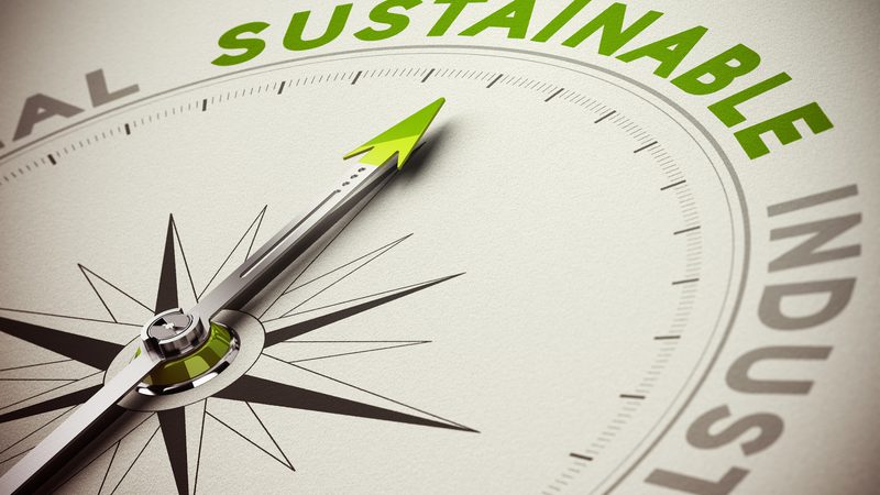A close-up of a compass pointing towards the word "SUSTAINABLE" on a gauge, with other words like "ALL" and "INDUSTRY" partially visible.
