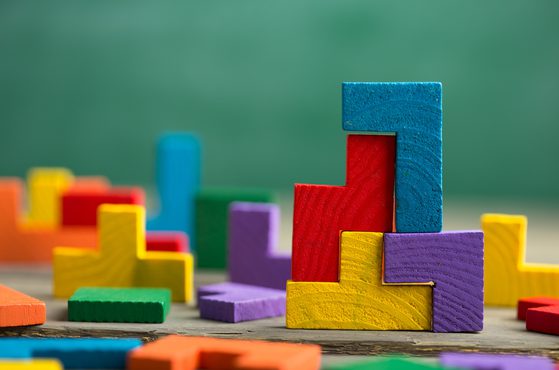 Colorful wooden building blocks arranged in a stepped pattern, with a blurred background of more scattered blocks on a wooden surface.