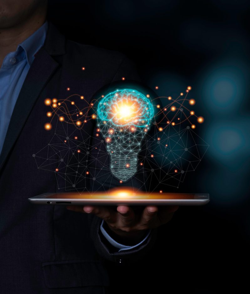 A person in a suit holding a tablet with a glowing, holographic lightbulb made of interconnected lines and nodes, symbolising innovation and ideas.