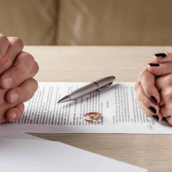 A divorcing couple sits across a table with divorce papers