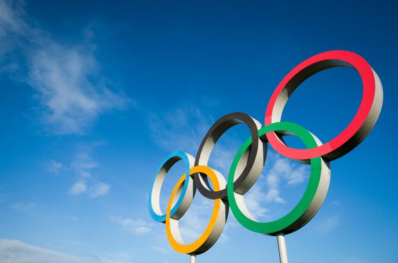 Olympic rings sculpture with five interlinked rings in blue, yellow, black, green, and red against a blue sky with some clouds.